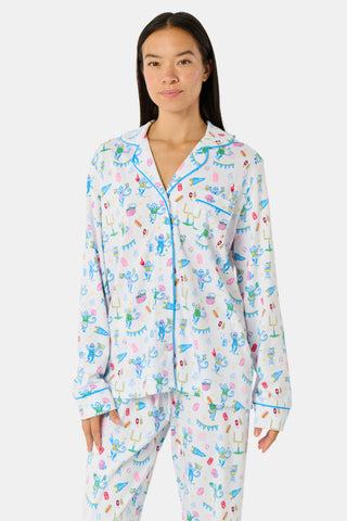 Roller Rabbit’s Game Day Long Sleeve Polo Pajamas feature a white button-up shirt and matching pants adorned with colorful, playful animal prints, festive bunting, and other cheerful designs.