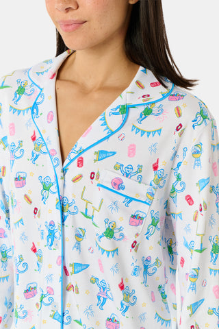 Roller Rabbit’s Game Day Long Sleeve Polo Pajamas feature a white button-up shirt and matching pants adorned with colorful, playful animal prints, festive bunting, and other cheerful designs.