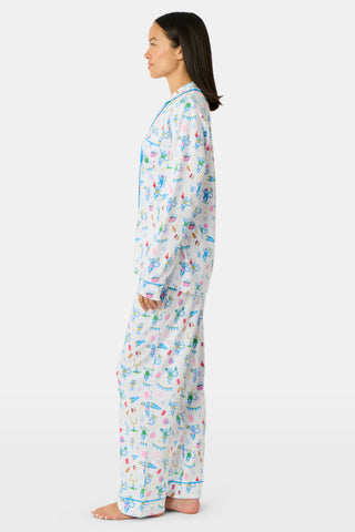 Roller Rabbit’s Game Day Long Sleeve Polo Pajamas feature a white button-up shirt and matching pants adorned with colorful, playful animal prints, festive bunting, and other cheerful designs.