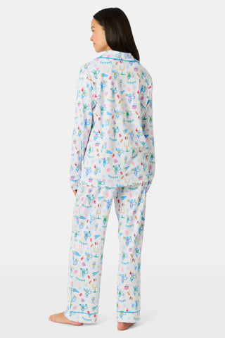 Roller Rabbit’s Game Day Long Sleeve Polo Pajamas feature a white button-up shirt and matching pants adorned with colorful, playful animal prints, festive bunting, and other cheerful designs.