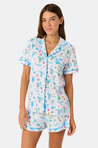 The Game Day Polo Pajamas by Roller Rabbit feature a short-sleeve button-up top and shorts, adorned with a lively pattern of colorful cartoon animals and party items on a white background.