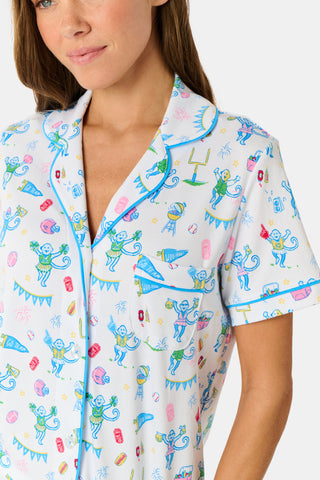 The Game Day Polo Pajamas by Roller Rabbit feature a short-sleeve button-up top and shorts, adorned with a lively pattern of colorful cartoon animals and party items on a white background.