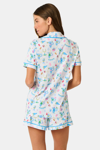 The Game Day Polo Pajamas by Roller Rabbit feature a short-sleeve button-up top and shorts, adorned with a lively pattern of colorful cartoon animals and party items on a white background.