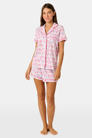 Introducing the Roller Rabbit Gamma Phi Beta Monkey Polo Pajamas: a short-sleeve Pima cotton set featuring a button-up top and matching shorts, adorned with a whimsical pink and blue monkey pattern and red trim on a crisp white background.