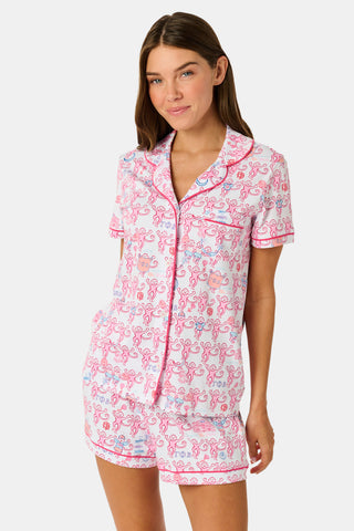 Introducing the Roller Rabbit Gamma Phi Beta Monkey Polo Pajamas: a short-sleeve Pima cotton set featuring a button-up top and matching shorts, adorned with a whimsical pink and blue monkey pattern and red trim on a crisp white background.