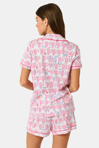 Introducing the Roller Rabbit Gamma Phi Beta Monkey Polo Pajamas: a short-sleeve Pima cotton set featuring a button-up top and matching shorts, adorned with a whimsical pink and blue monkey pattern and red trim on a crisp white background.