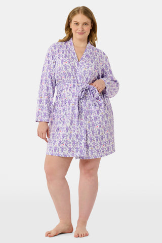 A woman smiles while wearing the TEXPIMA Get Ready With Me Blake Robe, featuring a knee-length cut and a purple and pink paisley pattern, tied at the waist, against a plain white background.