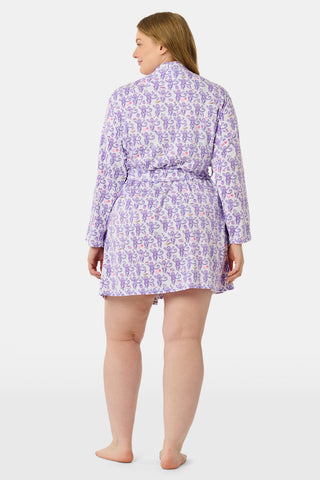 A woman smiles while wearing the TEXPIMA Get Ready With Me Blake Robe, featuring a knee-length cut and a purple and pink paisley pattern, tied at the waist, against a plain white background.