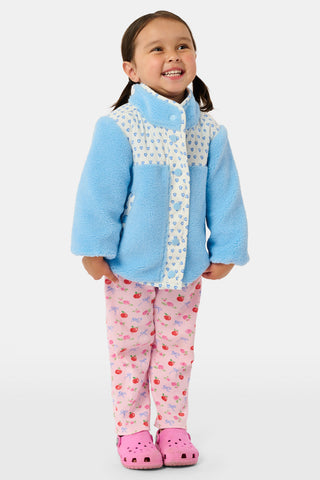 A young girl stands and smiles against a plain background, wearing the Roller Rabbit Kids Hearts Lizzie Fleece Jacket in light blue with white patterned details, paired with matching white leggings adorned with blue hearts. This cozy outerwear features soft fleece for comfort and warmth.