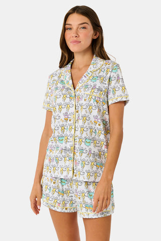The Kappa Alpha Theta Monkey Polo Pajamas from Roller Rabbit are a short-sleeve button-up set with matching shorts, showcasing a lively print of colorful cartoon monkeys and doodles on a crisp white background. They feature an elastic waistband for comfort and are crafted from soft Pima cotton for a gentle feel.