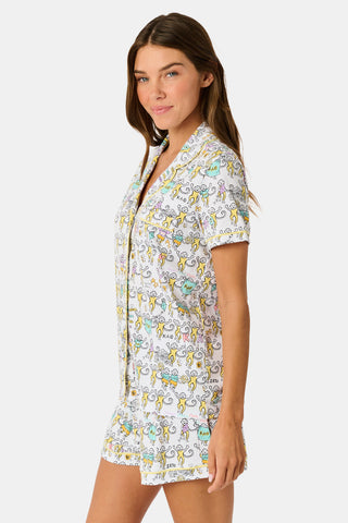 The Kappa Alpha Theta Monkey Polo Pajamas from Roller Rabbit are a short-sleeve button-up set with matching shorts, showcasing a lively print of colorful cartoon monkeys and doodles on a crisp white background. They feature an elastic waistband for comfort and are crafted from soft Pima cotton for a gentle feel.