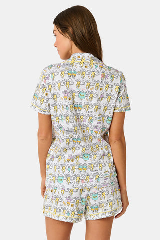 The Kappa Alpha Theta Monkey Polo Pajamas from Roller Rabbit are a short-sleeve button-up set with matching shorts, showcasing a lively print of colorful cartoon monkeys and doodles on a crisp white background. They feature an elastic waistband for comfort and are crafted from soft Pima cotton for a gentle feel.