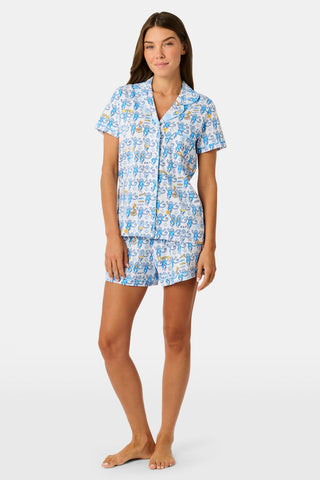 The Roller Rabbit Kappa Kappa Gamma Monkey Polo Pajamas feature a short-sleeve button-up pajama shirt with a front button placket and matching shorts with an elastic waistband, adorned with a playful blue monkey and yellow motif on a white background. Crafted from soft Pima cotton for extra comfort.