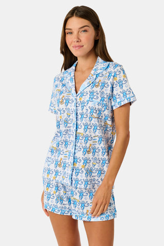 The Roller Rabbit Kappa Kappa Gamma Monkey Polo Pajamas feature a short-sleeve button-up pajama shirt with a front button placket and matching shorts with an elastic waistband, adorned with a playful blue monkey and yellow motif on a white background. Crafted from soft Pima cotton for extra comfort.
