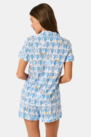 The Roller Rabbit Kappa Kappa Gamma Monkey Polo Pajamas feature a short-sleeve button-up pajama shirt with a front button placket and matching shorts with an elastic waistband, adorned with a playful blue monkey and yellow motif on a white background. Crafted from soft Pima cotton for extra comfort.