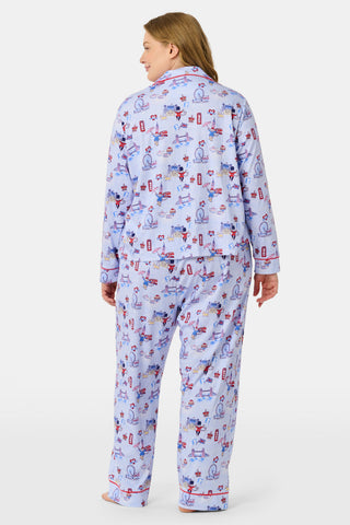 A young child with curly hair stands barefoot against a plain white background, wearing Roller Rabbit’s Kids London Monkey Pajamas—light blue long-sleeve pajamas adorned with playful, colorful patterns featuring guards, clocks, and iconic British landmarks.