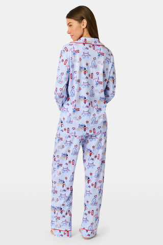A young child with curly hair stands barefoot against a plain white background, wearing Roller Rabbit’s Kids London Monkey Pajamas—light blue long-sleeve pajamas adorned with playful, colorful patterns featuring guards, clocks, and iconic British landmarks.