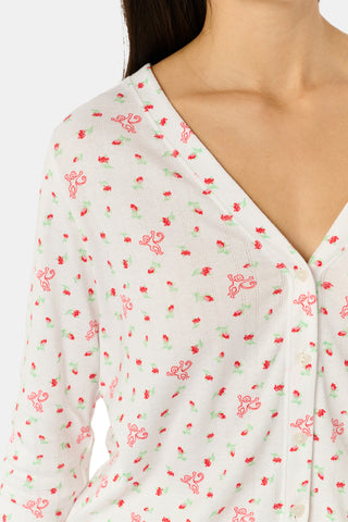 A woman wearing the Roller Rabbit Mini Monkey Blossom Pointelle Allie V-Neck Cardigan—a long-sleeve, white pajama top featuring a small pink floral print and crafted from soft Pima cotton—stands against a plain white background, smiling gently.