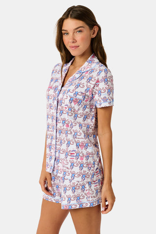 The Roller Rabbit Pi Beta Phi Monkey Polo Pajamas feature a short-sleeved button-up top and matching shorts, adorned with a playful pink and blue monkey print on a white background. Crafted from soft Pima cotton with an elastic waistband for comfort, these pajamas are made in Peru.