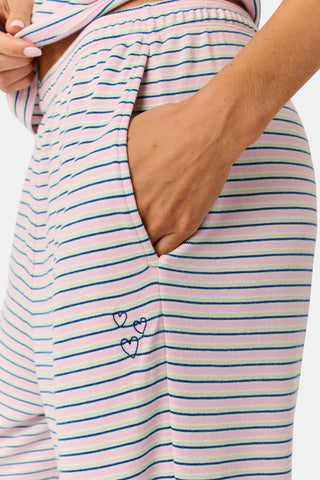 A person stands barefoot on a white background wearing the Roller Rabbit Striped Eva Pant—loose, light-colored pima cotton pajama pants featuring thin blue and red horizontal stripes. Their top is lifted slightly, revealing the elastic waistband.