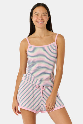 A woman smiles while wearing the Roller Rabbit Striped Lia Set, which features a sleeveless, pink and white striped Pima cotton tank with adjustable straps and matching shorts with ruffled hems and an elastic waistband, standing against a plain light background.