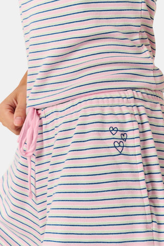 A woman smiles while wearing the Roller Rabbit Striped Lia Set, which features a sleeveless, pink and white striped Pima cotton tank with adjustable straps and matching shorts with ruffled hems and an elastic waistband, standing against a plain light background.