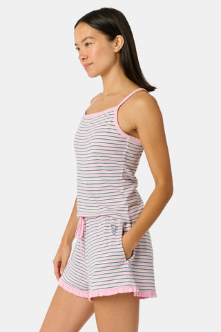 A woman smiles while wearing the Roller Rabbit Striped Lia Set, which features a sleeveless, pink and white striped Pima cotton tank with adjustable straps and matching shorts with ruffled hems and an elastic waistband, standing against a plain light background.