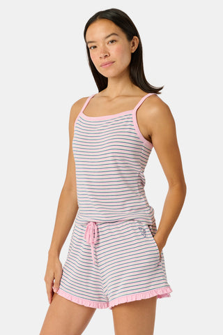 A woman smiles while wearing the Roller Rabbit Striped Lia Set, which features a sleeveless, pink and white striped Pima cotton tank with adjustable straps and matching shorts with ruffled hems and an elastic waistband, standing against a plain light background.