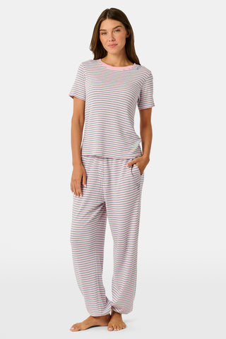 A woman wearing the Roller Rabbit Striped Steph Tee—a short-sleeve, white Pima Cotton pajama top featuring thin horizontal navy and pink stripes and a light pink collar—stands against a plain background.