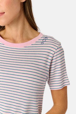 A person stands barefoot on a white background wearing the Roller Rabbit Striped Eva Pant—loose, light-colored pima cotton pajama pants featuring thin blue and red horizontal stripes. Their top is lifted slightly, revealing the elastic waistband.