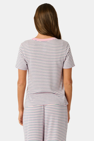 A woman wearing the Roller Rabbit Striped Steph Tee—a short-sleeve, white Pima Cotton pajama top featuring thin horizontal navy and pink stripes and a light pink collar—stands against a plain background.
