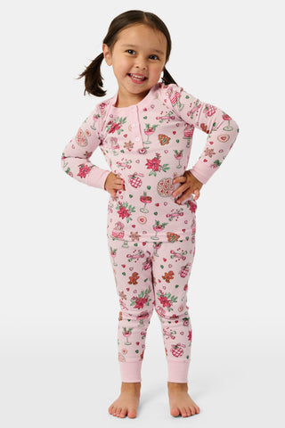 A child in a patterned Kids Seasons Soiree Juniper Pajamas two-piece set and rubber boots sits on a wooden sled and looks through binoculars.