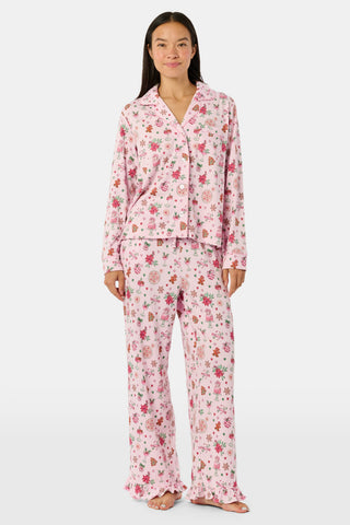 A person wearing pink long-sleeved Seasons Soiree Kate Pajamas with a ruffled hem and a repeating print of holiday sweets and treats.