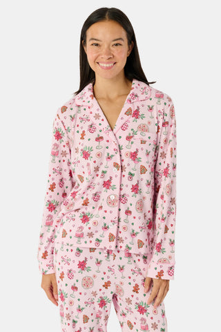 A person wearing pink long-sleeved Seasons Soiree Kate Pajamas with a ruffled hem and a repeating print of holiday sweets and treats.