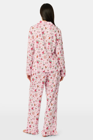 A person wearing pink long-sleeved Seasons Soiree Kate Pajamas with a ruffled hem and a repeating print of holiday sweets and treats.