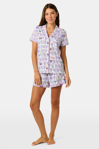 The Sigma Kappa Monkey Polo Pajamas by Roller Rabbit are a short-sleeve pajama set featuring matching shorts with a white background and colorful cartoon character pattern. Designed for comfort, they include a front button placket and an elastic waistband.
