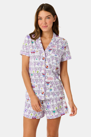 The Sigma Kappa Monkey Polo Pajamas by Roller Rabbit are a short-sleeve pajama set featuring matching shorts with a white background and colorful cartoon character pattern. Designed for comfort, they include a front button placket and an elastic waistband.