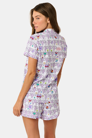The Sigma Kappa Monkey Polo Pajamas by Roller Rabbit are a short-sleeve pajama set featuring matching shorts with a white background and colorful cartoon character pattern. Designed for comfort, they include a front button placket and an elastic waistband.
