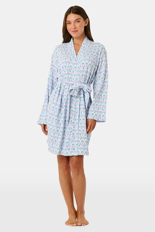 A woman wears a knee-length SERFLEX Snowday Stripe Piper Robe featuring horizontal rows of winter-themed snowflakes, hearts, and stars in shades of blue, pink, and green.