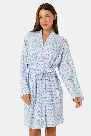 A woman wears a knee-length SERFLEX Snowday Stripe Piper Robe featuring horizontal rows of winter-themed snowflakes, hearts, and stars in shades of blue, pink, and green.
