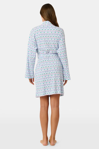 A woman wears a knee-length SERFLEX Snowday Stripe Piper Robe featuring horizontal rows of winter-themed snowflakes, hearts, and stars in shades of blue, pink, and green.
