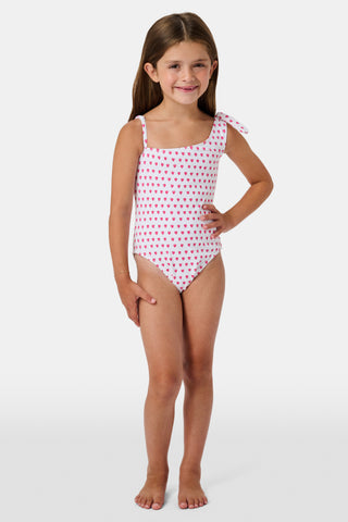 The Roller Rabbit Hearts Kids Jacey One Piece is a swimsuit with an asymmetrical neckline, white fabric dotted with pink hearts, and an adjustable knot-tied shoulder strap.