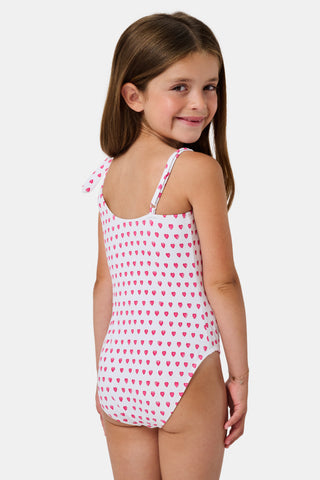 The Roller Rabbit Hearts Kids Jacey One Piece is a swimsuit with an asymmetrical neckline, white fabric dotted with pink hearts, and an adjustable knot-tied shoulder strap.