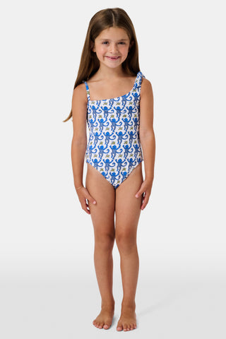 The Monkey Kids Jacey One Piece by Roller Rabbit is a white, one-shoulder swimsuit with blue monkeys and yellow bananas. It features an asymmetrical neckline, a knotted right tie strap, and playful monkey illustrations.