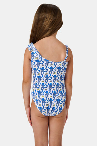 The Monkey Kids Jacey One Piece by Roller Rabbit is a white, one-shoulder swimsuit with blue monkeys and yellow bananas. It features an asymmetrical neckline, a knotted right tie strap, and playful monkey illustrations.