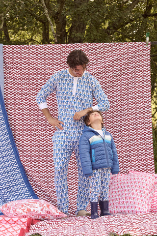 A child wears a blue SOPHISTICA Kids Monkey Reversible Puffer Jacket featuring heart-shaped quilting, a white and light blue chest stripe, and a hood.