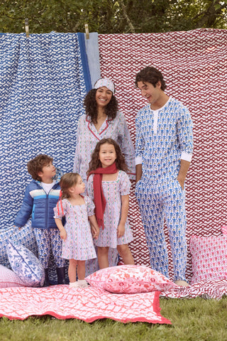 A girl wears the SANSKRITI Kids Mistletoe Stripe Lottie Dress in a blue and white-striped cotton print with puff sleeves, a square neckline, and red heart accents, paired with blue velvet Mary Jane flats.