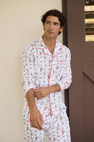 A woman wears a SERFLEX Deck The Halls Bailey Pajamas set featuring a short-sleeved top and shorts with a white background and a repeating Christmas-themed pattern of elves, snowmen, and evergreen trees.