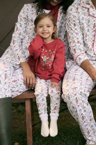 A child wears a Kids Deck The Halls Andie Sweatshirt featuring a heart made of festive lights, a cartoon monkey, and a Christmas tree graphic, paired with patterned leggings showing elves and snowmen.