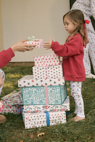 A child wears a Kids Deck The Halls Andie Sweatshirt featuring a heart made of festive lights, a cartoon monkey, and a Christmas tree graphic, paired with patterned leggings showing elves and snowmen.